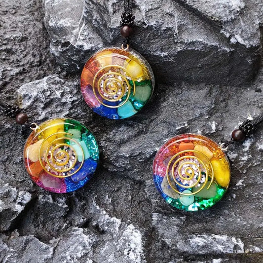 Three colorful rainbow chakra healing pendants with spiral design on textured stone background.