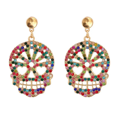 Close-up of gold skull-shaped dangle earrings with multicolored rhinestones on a gray background.