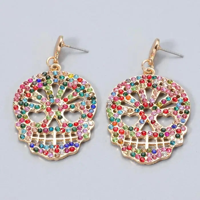 Gold skull-shaped dangle earrings decorated with multicolored rhinestones on a white background.