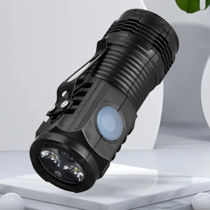 Black compact LED flashlight displayed on a minimalist white platform with a modern background.