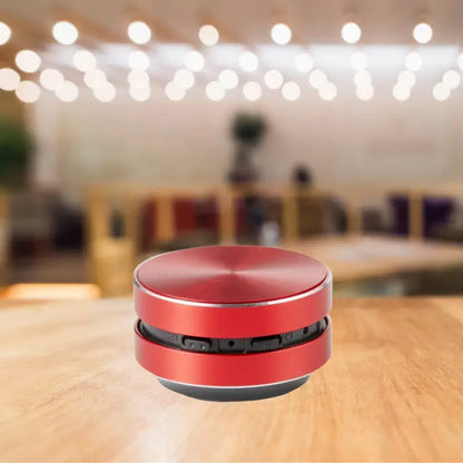 compact red bluetooth speaker with metallic finish displayed on wooden table with ambient bokeh lighting effect