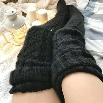 Black knit socks on feet, white lantern and candles in background, creating a cozy atmosphere on textured fabric