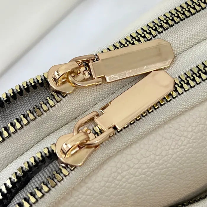 Close-up of gold zipper details on a cream bag, emphasizing its premium craftsmanship and design.