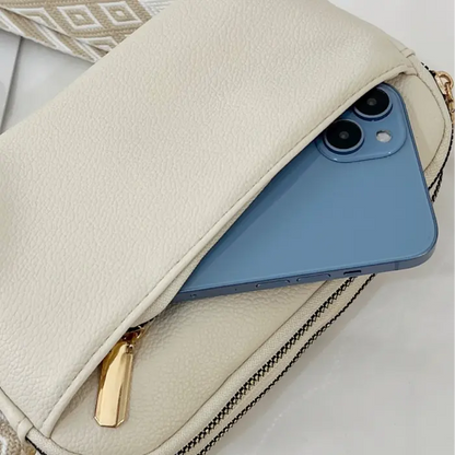 Cream crossbody bag holding a phone securely in its front pocket, ideal for modern convenience.