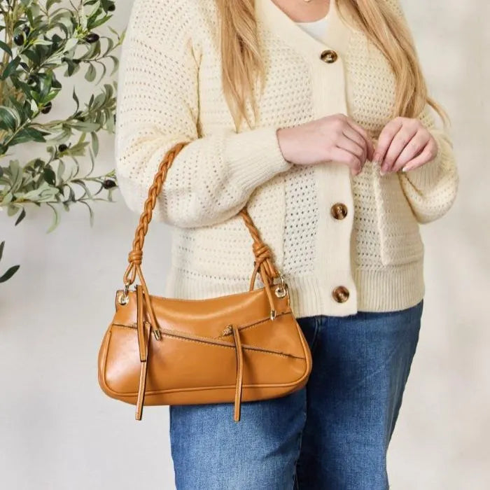 Styled shot of camel leather handbag paired with cream knit cardigan, showing decorative zipper details and braided strap