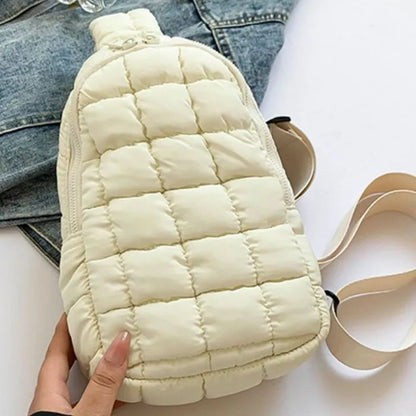 Cream quilted sling bag with zipper closure and adjustable strap, displayed on denim jacket background