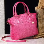 Crocodile embossed handbag in bubblegum pink with matching strap, gold accents, and pebbled background.