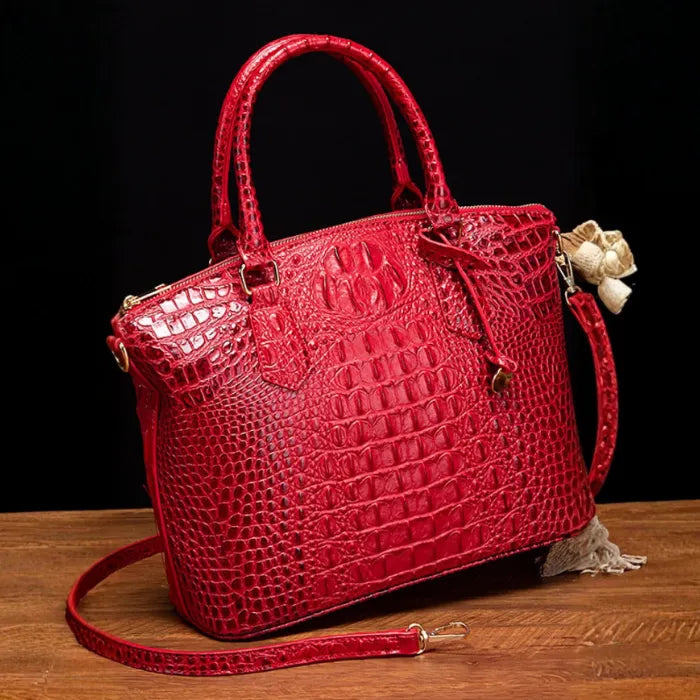 Crocodile embossed handbag in classic red with glossy finish and gold zipper, styled on rustic wood.
