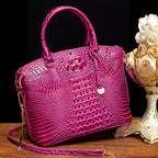 Crocodile embossed handbag in glossy hot pink with gold charm and detachable shoulder strap on wood surface.