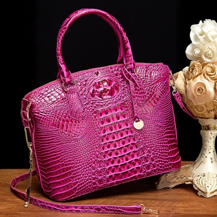 Crocodile embossed handbag in glossy hot pink with gold charm and detachable shoulder strap on wood surface.