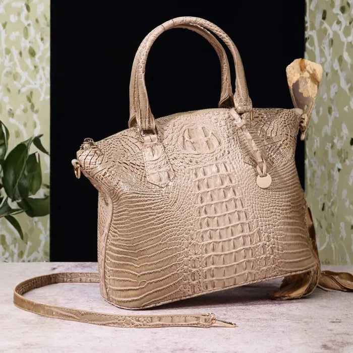 Crocodile embossed handbag in light beige tone with soft gloss and structured silhouette on neutral backdrop.