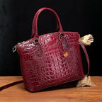 Crocodile embossed handbag in wine red with sleek silhouette and gold charm against elegant decor