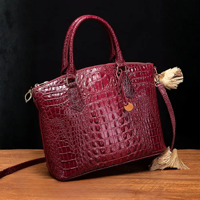 Crocodile embossed handbag in wine red with sleek silhouette and gold charm against elegant decor