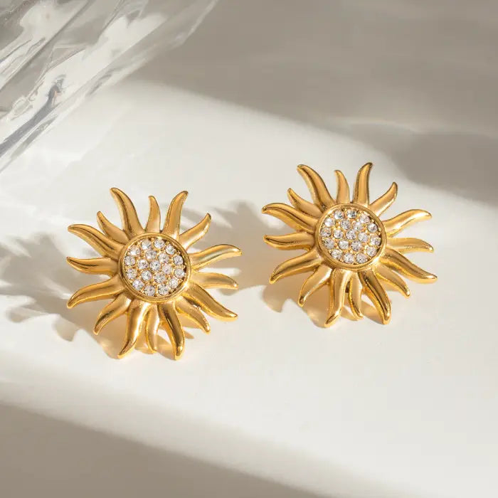 Crystal-embellished gold sun earrings displayed on a glossy surface.