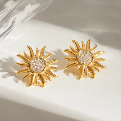 Crystal-embellished gold sun earrings displayed on a glossy surface.