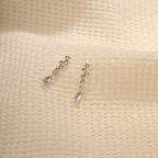 crystal teardrop dangle earrings in silver placed on textured cream fabric, shimmering rhinestone design offering elegant lightweight sparkle