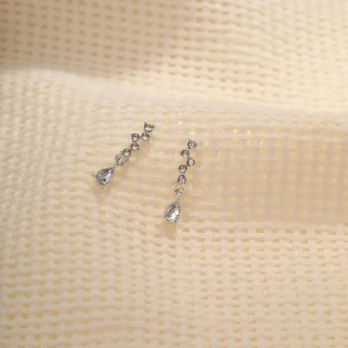 crystal teardrop dangle earrings in silver placed on textured cream fabric, shimmering rhinestone design offering elegant lightweight sparkle