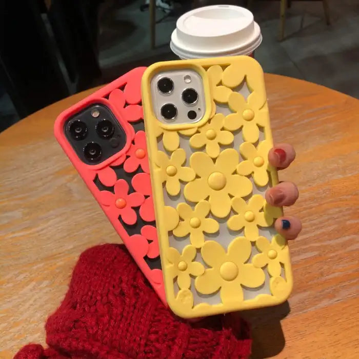 Cute floral iPhone case in yellow and coral colors with 3D daisy cutout design displayed on wooden table