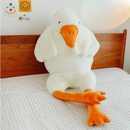 Adorable white duck plush toy sitting on a bed with orange feet.