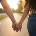 dainty gold heart chain bracelet worn by woman while holding hands at sunset, creating a warm romantic moment and elegant jewelry appeal