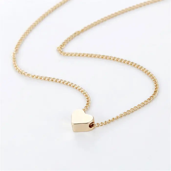 Delicate gold chain necklace featuring a small polished heart pendant on white background