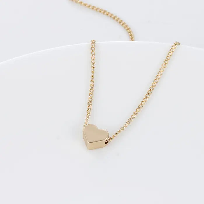 Gold heart charm necklace laid flat on white textured surface with soft lighting