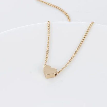 Gold heart charm necklace laid flat on white textured surface with soft lighting