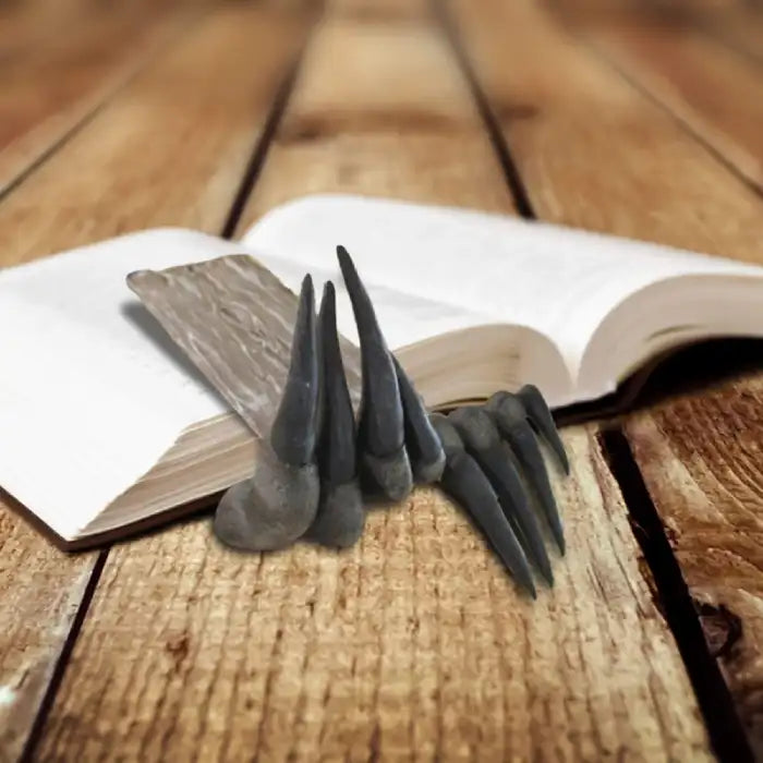 Decorative sculpture bookmark shaped like dinosaur hand placed inside open book on wood floor.