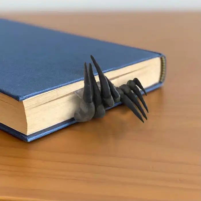 Decorative sculpture claw bookmark sticking out from blue hardcover book on wooden surface.