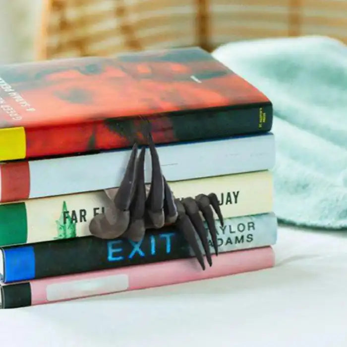 Decorative sculpture claw bookmark placed between stacked books on a bed with soft background.