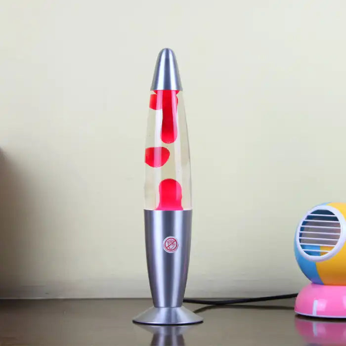 Decorative wax lamp with red wax in a silver base on a desk beside a colorful mini fan.