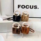 Four mini bucket bags in black, beige, brown, and tan arranged on clear display with FOCUS text background