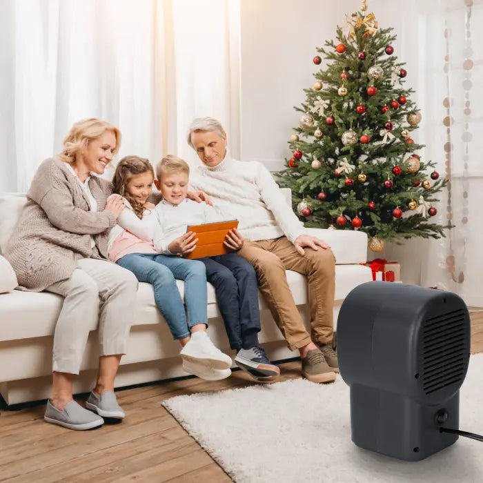 Desktop electric heater warming family in cozy living room beside decorated Christmas tree.