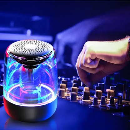 Hand adjusting DJ mixer controls next to illuminated wireless speaker with blue and pink lights in dark setting