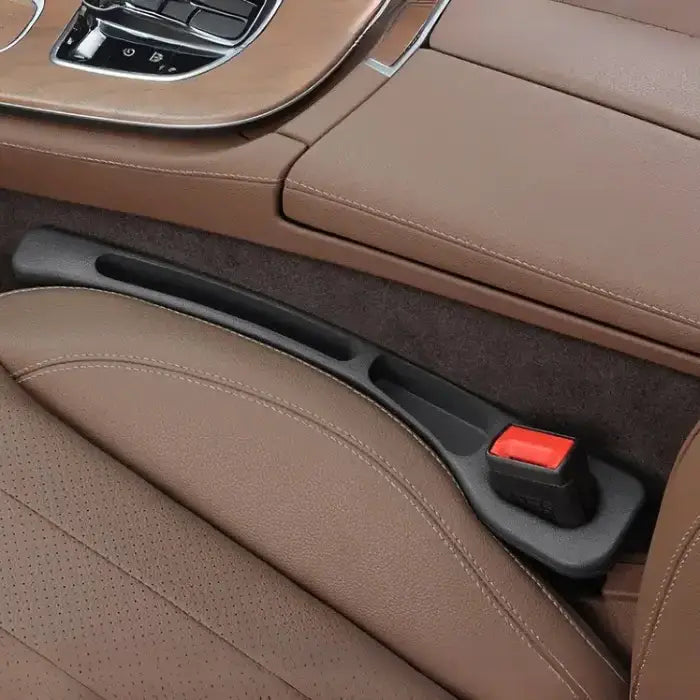 Driver side black plastic car seat gap filler installed between brown leather seats with chrome console trim