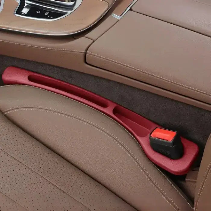 Driver side red plastic car seat gap filler installed between brown leather seats with chrome console trim