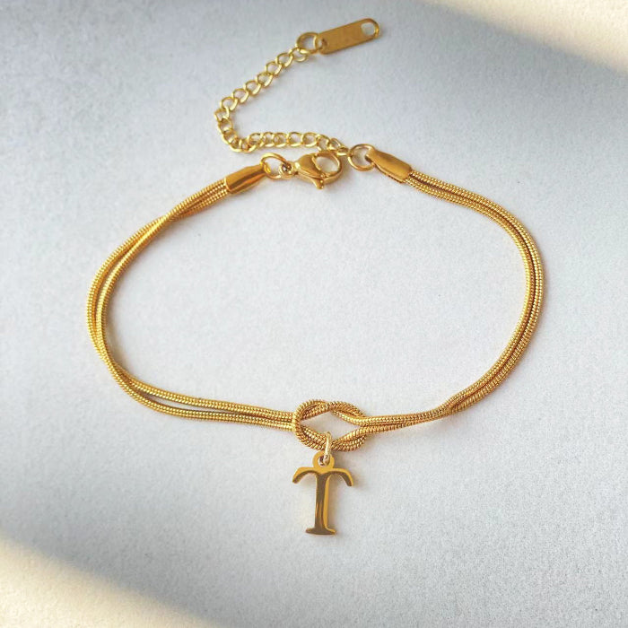 Gold bracelet with a letter 'T' charm on a light gray background