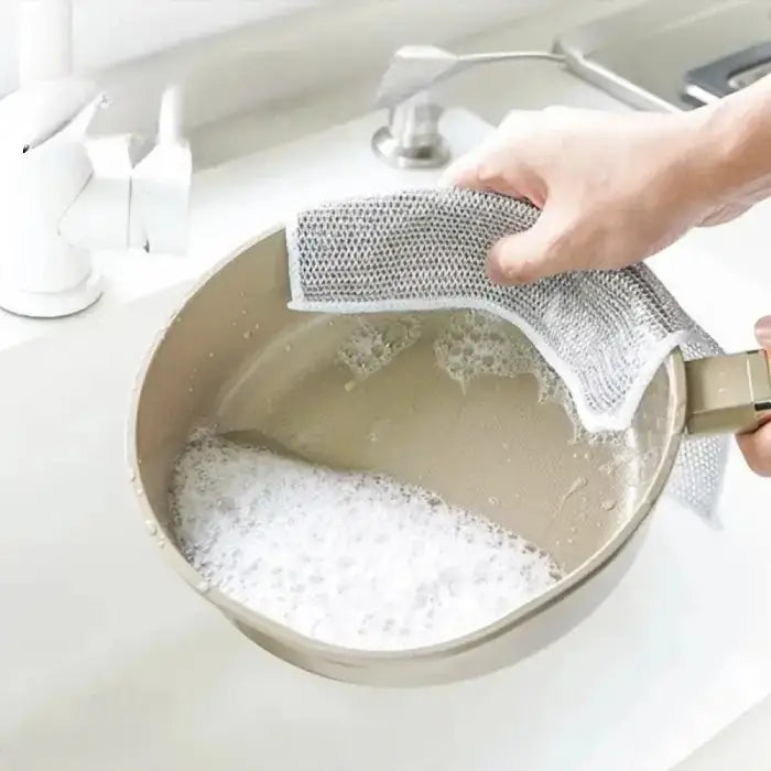 hand cleaning a nonstick pan with a soapy sponge in a sink