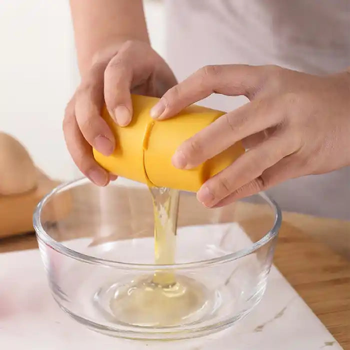 Egg shell opener being squeezed to release raw egg whites into a glass mixing bowl.