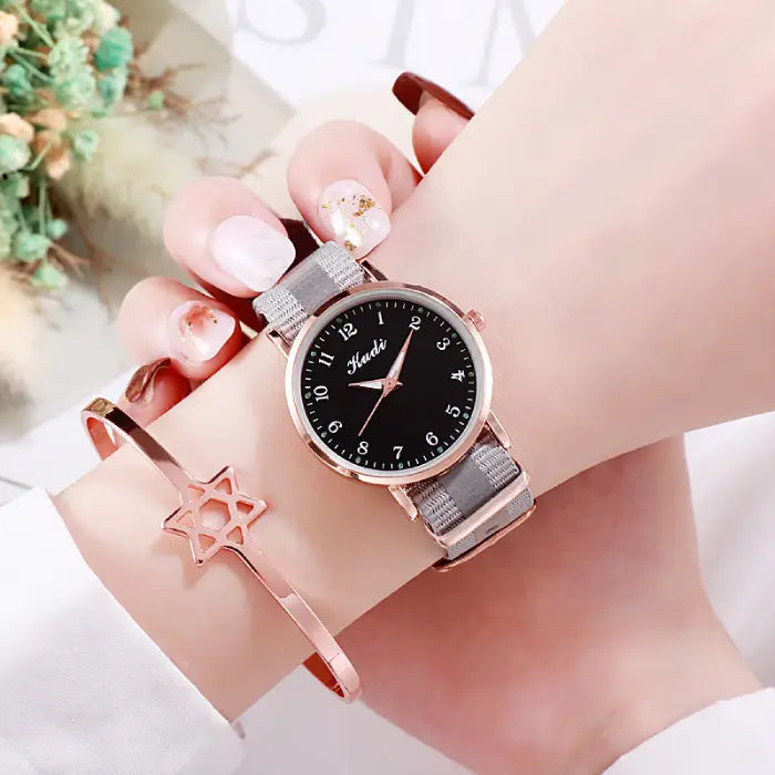 Women's watch with a black dial and gray strap paired with a rose gold bracelet featuring a star design.