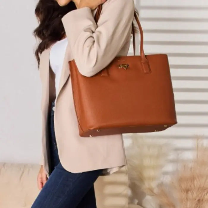 Woman carrying brown leather tote bag, wearing beige coat and jeans, standing against white paneled wall