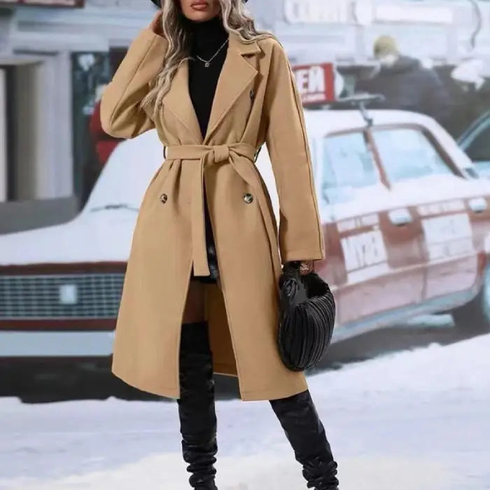 Stylish camel trench coat with belt tie, worn with black turtleneck and boots, accessorized with black handbag in winter setting