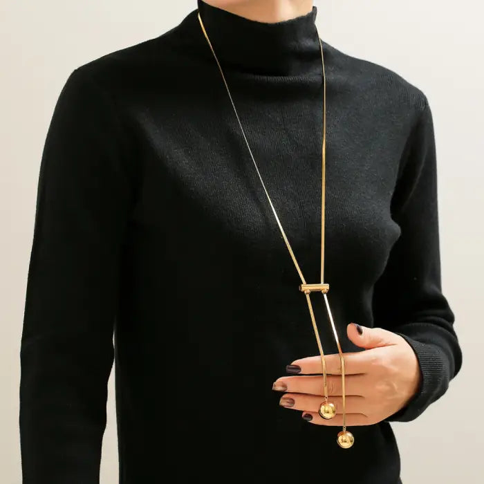 Gold double-ball pendant necklace styled with black turtleneck sweater, showing modern minimalist design