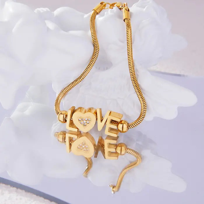 Gold-plated LOVE bracelet with crystal heart displayed on white surface with mirror reflection