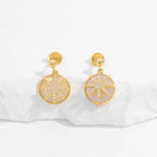 Gold starburst drop earrings with crystal details displayed on white textured surface with soft shadows