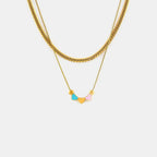 A delicate golden necklace with three heart-shaped pendants in blue, yellow, and pink colors on a plain white background