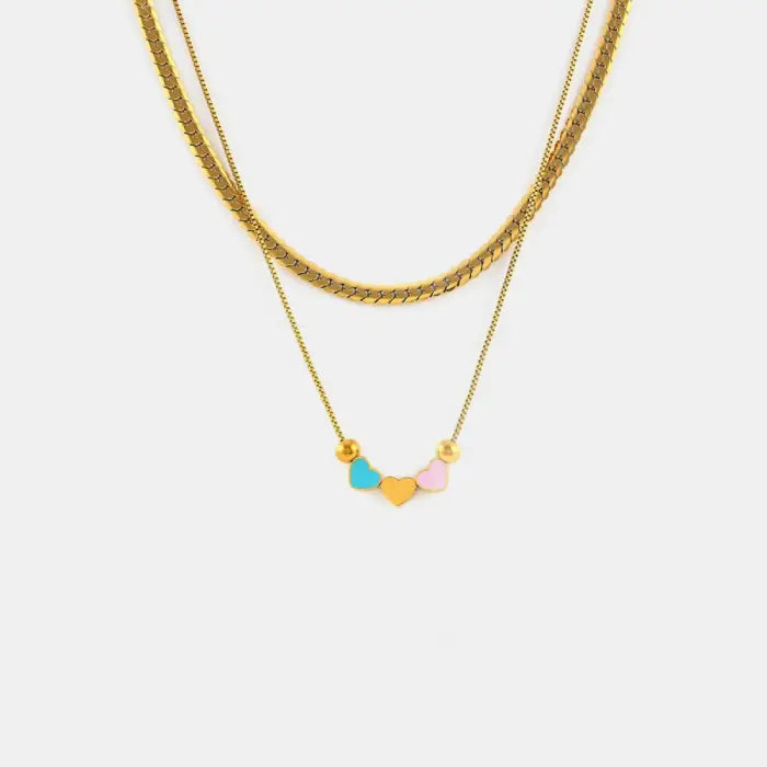 A delicate golden necklace with three heart-shaped pendants in blue, yellow, and pink colors on a plain white background