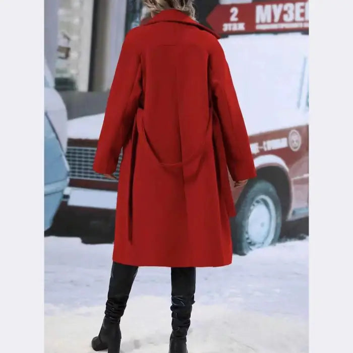 Back view of a long red wool coat paired with black knee-high boots against a snowy winter street backdrop