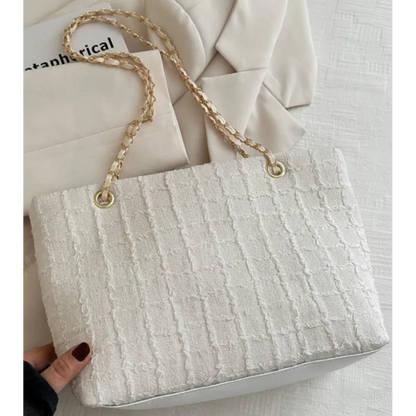 Elegant cream textured tote bag with gold chain strap on light background