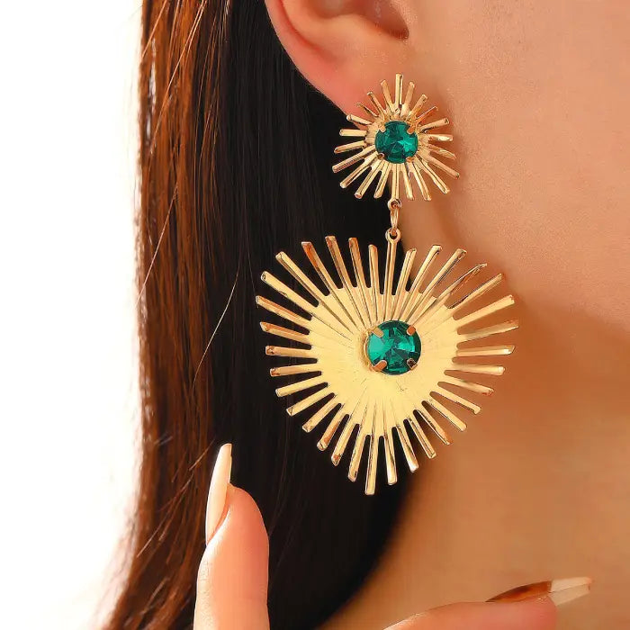 emerald sunburst statement earrings in gold worn on ear, featuring bright green crystals and bold sunray spokes for luxury styling